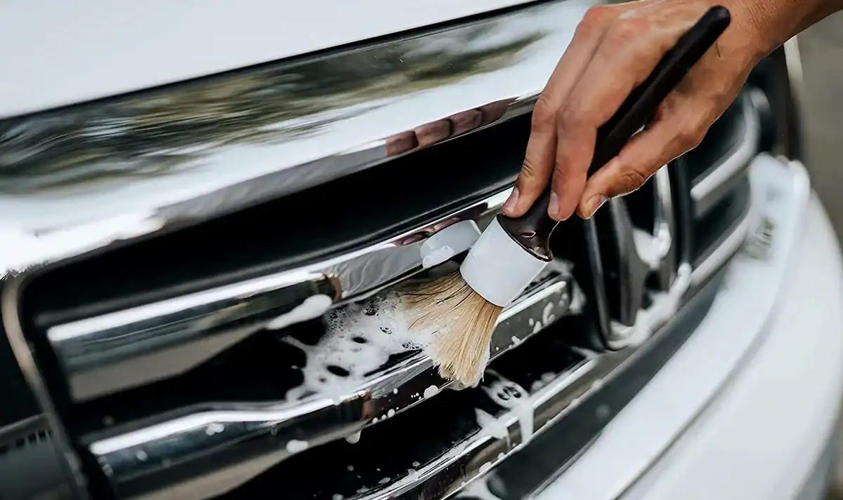 Primer plano de una mano utilizando un cepillo detallado con jabón para limpiar la parrilla de un coche, haciendo hincapié en la limpieza de precisión.