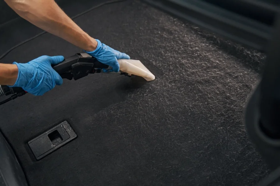 Person wearing blue gloves using vacuum to clean car floor interior, focusing on thorough dust and dirt removal.