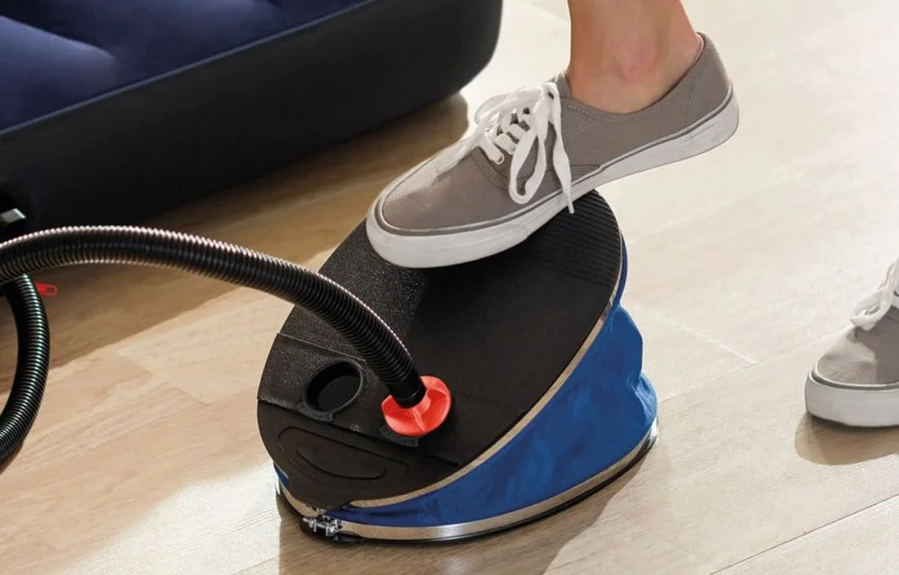 Person using a foot pump to inflate an air mattress indoors.