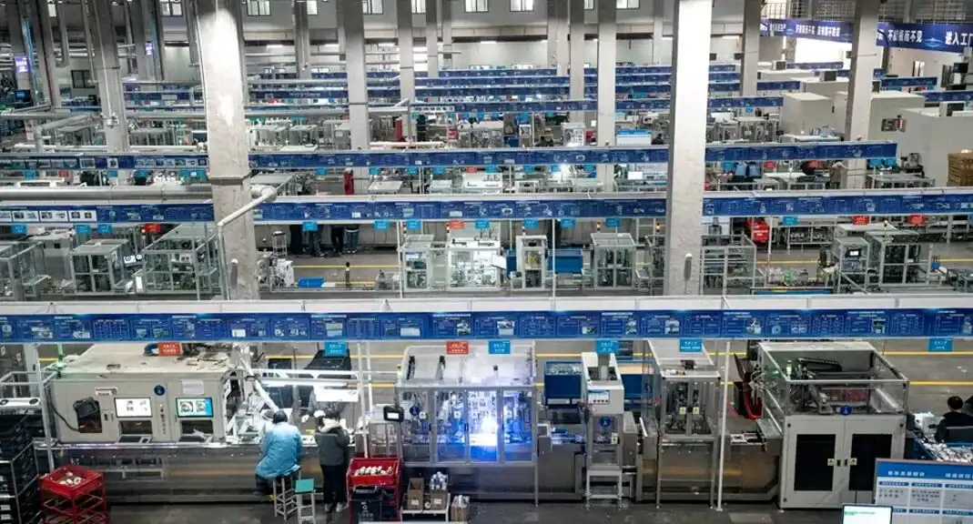 A sprawling industrial factory with rows of automation equipment and workers operating machinery under well-lit conditions.