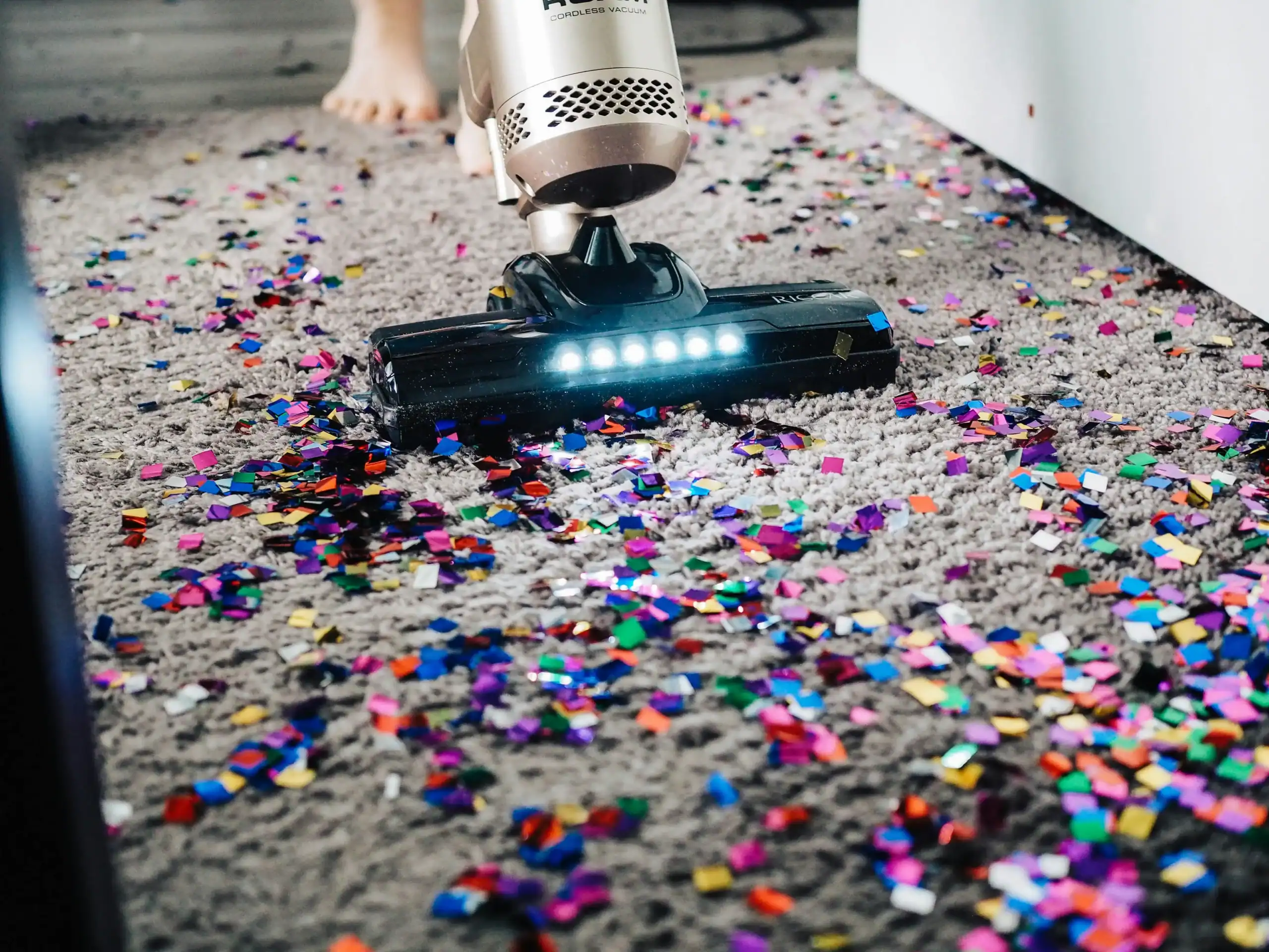 Vacuum cleaner cleaning up colorful confetti on carpet, showcasing car accessory functionality.