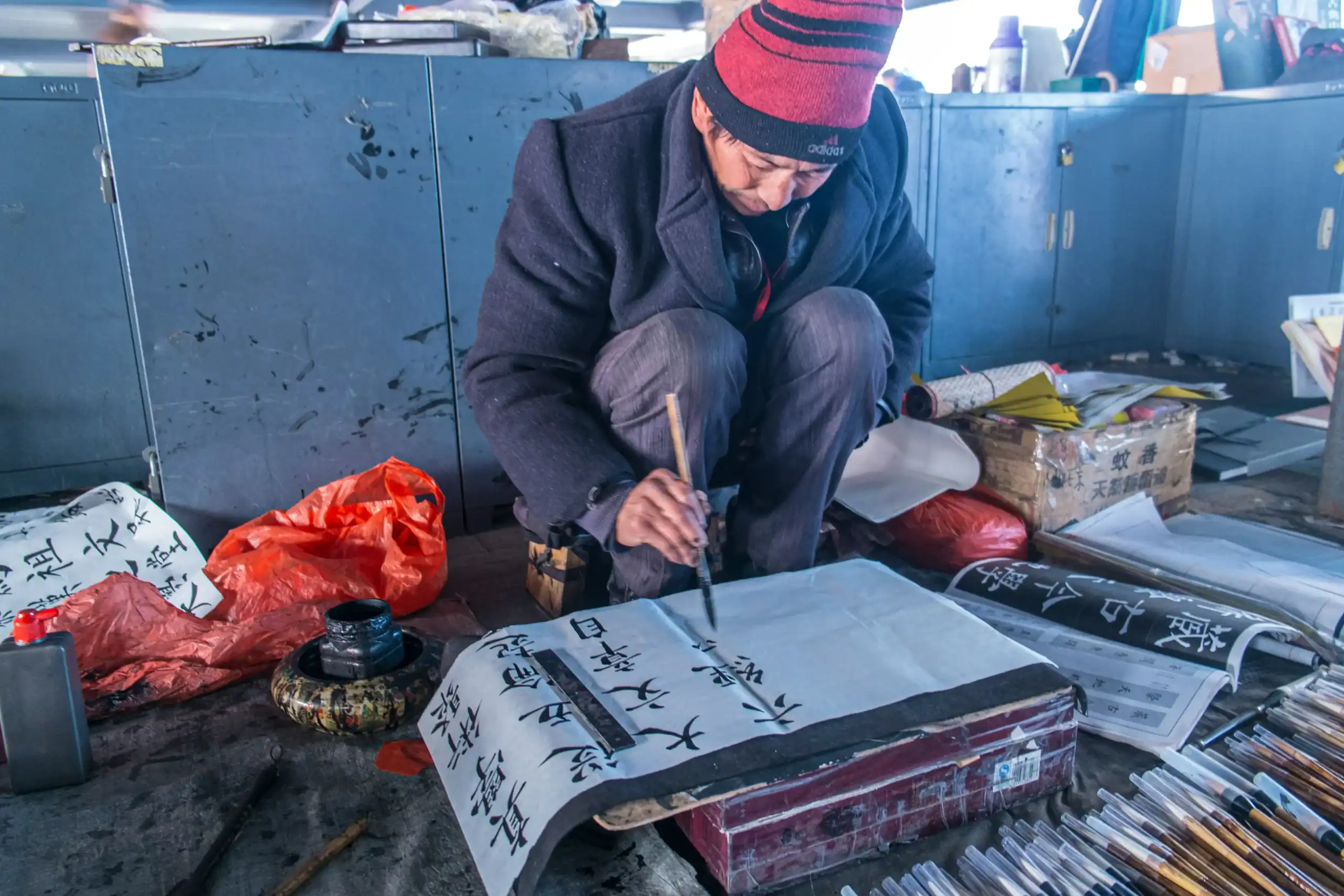 Man writing calligraphy on paper with traditional tools.