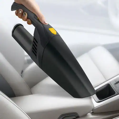 Compact handheld car vacuum cleaner being used to clean a car seat area, featuring a sleek black design with a yellow button.
