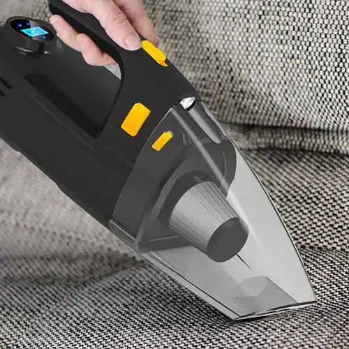 A handheld vacuum cleaner with a clear nozzle being used to clean a textured fabric surface, showing a digital display on top.