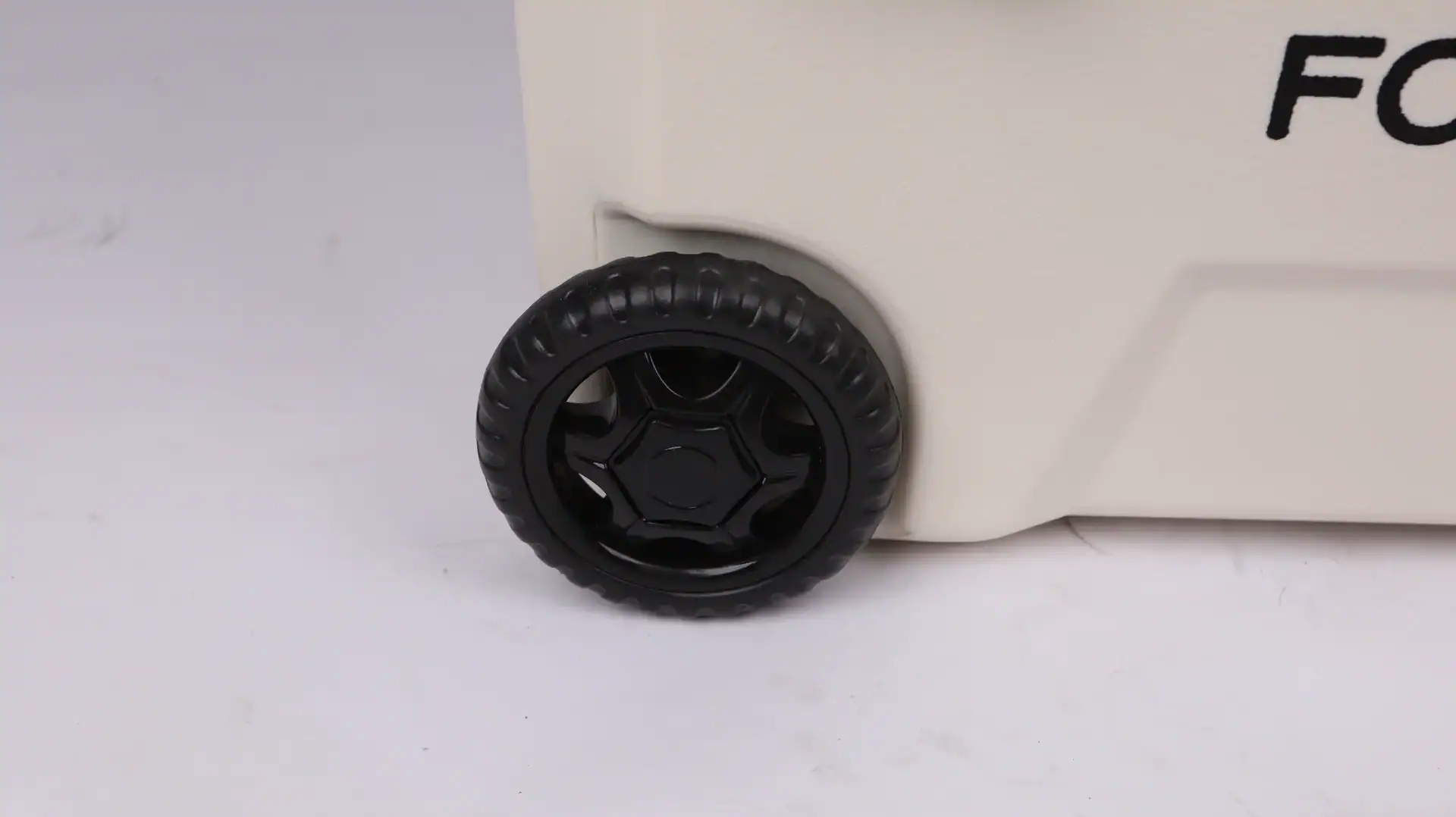 Close-up of a sturdy black plastic wheel attached to a cream-colored portable cooler, designed for easy transportation.