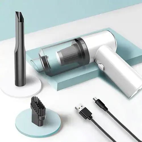 Compact white portable handheld vacuum cleaner with a transparent dust container, shown with cleaning attachments and USB charging cable on a modern surface.