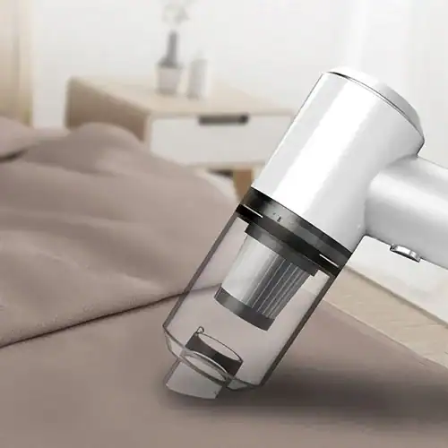 Sleek white portable handheld vacuum cleaner with a transparent dust collector being used on a fabric surface in a modern room.