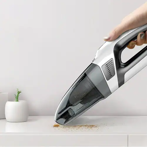Person using a portable handheld vacuum cleaner to clean a white surface with dust particles near small potted plants.