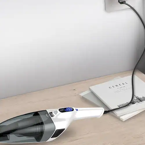 A sleek, portable handheld vacuum cleaner plugged into a wall socket, resting on a wooden table beside neatly arranged magazines.