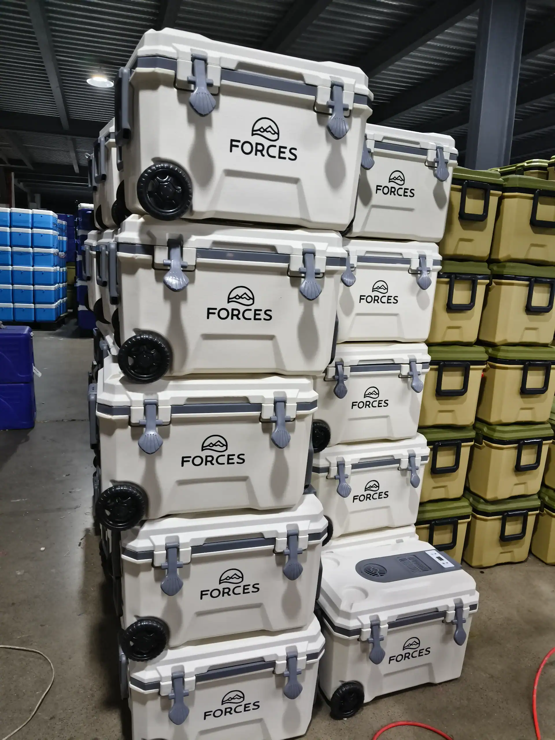 Multiple white and beige portable coolers branded 'FORCES' stacked in a warehouse with a high ceiling. A cooling unit is visible.