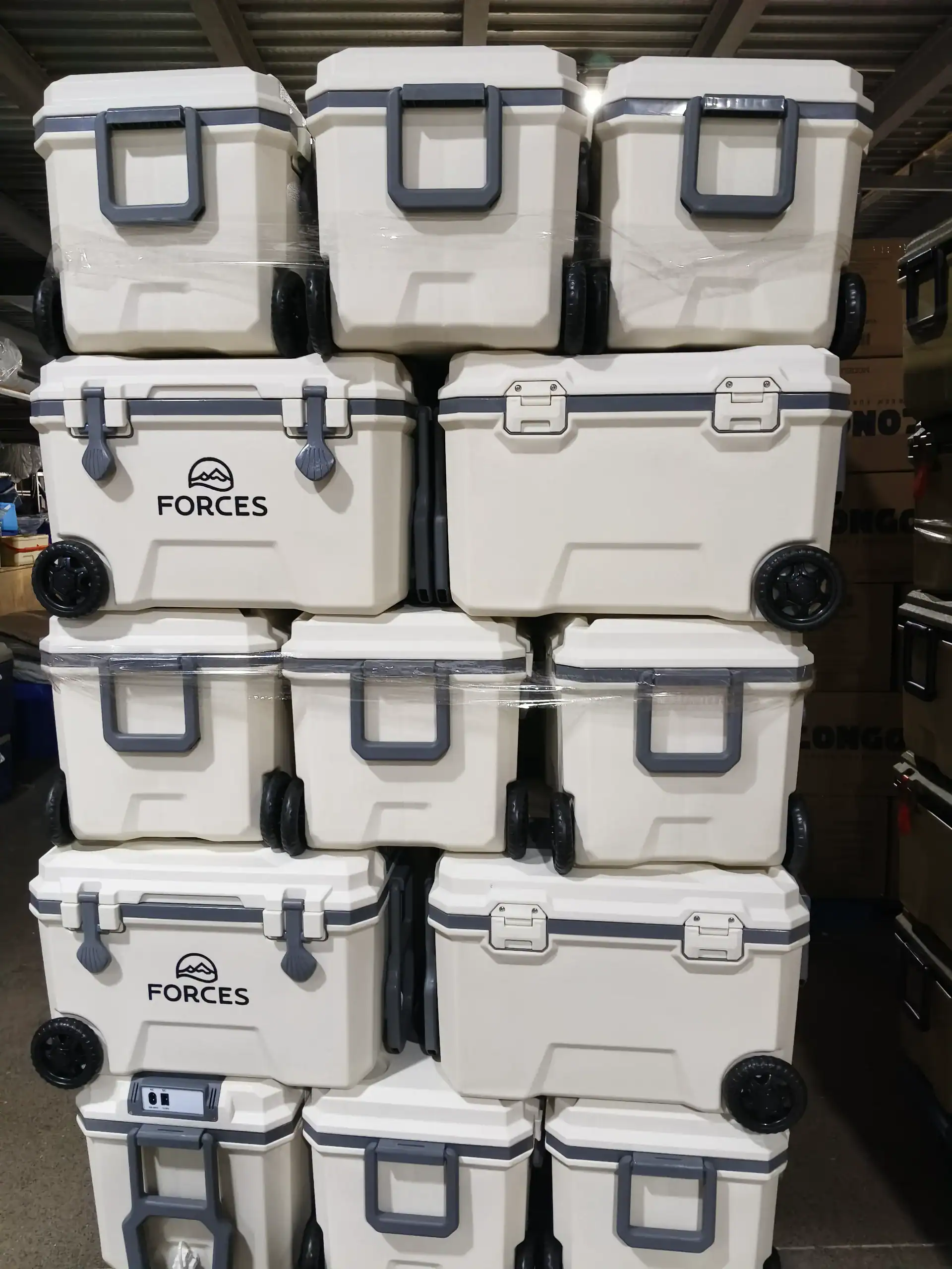Pallet of white cooler boxes with wheels and gray handles stacked neatly in a warehouse setting.